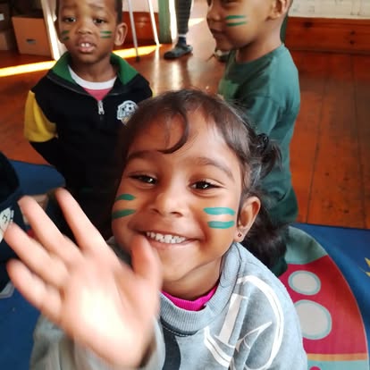Child with green face paint stripes waving at the camera