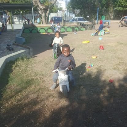 Two children playing with push-along bikes on a dirt playground