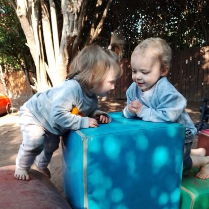 Two toddlers interacting over a blue sensory cube